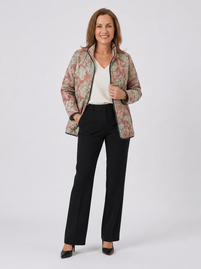 Woman wearing the Georgina quilted terracotta damask jacket open over an ivory top with black trousers